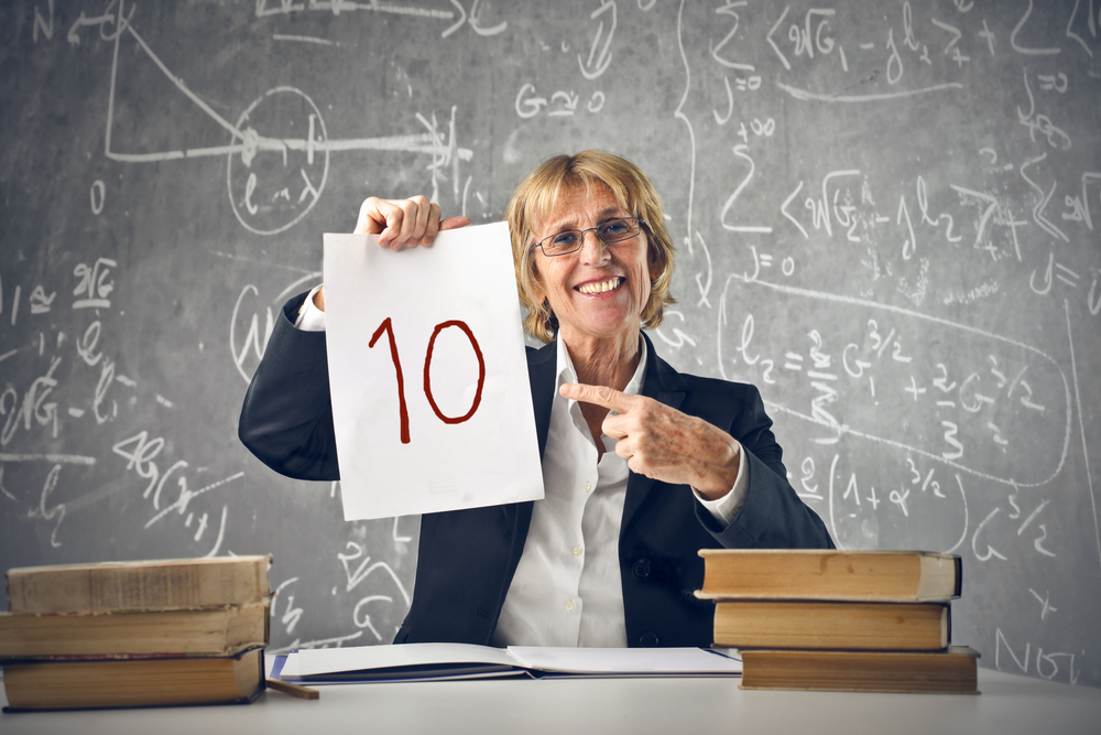 professoressa seduta alla scrivania che mostra un foglio su cui è scritto il numero 10 in rosso
